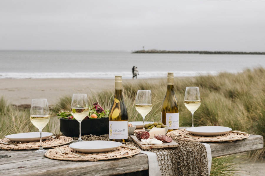 A picnic table with food and wine beside a quiet beach